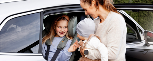 Kind sitzt im Kindersitz und Mutter hält ein Baby bei ihr